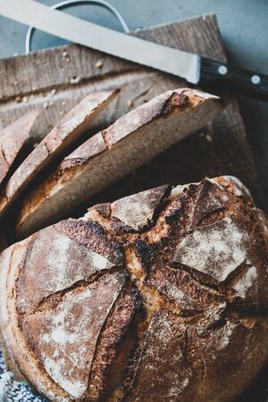 Flat-lay of freshly baked sourdough bread loaf on rustic wooden board over grey concrete table background, top viewの写真素材