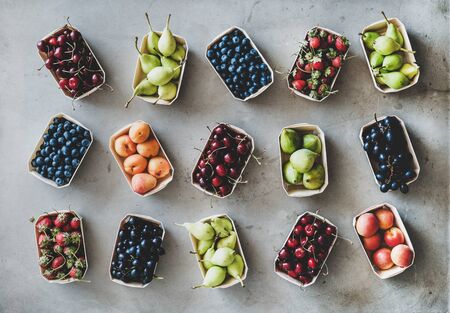 Summer fruit, berry assortment. Flat-lay of strawberries, cherries, grape, blueberries, pears, apricots, figs in eco-friendly boxes over grey background, top view. Local farmers market organic produceの写真素材