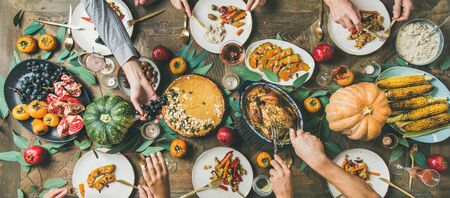 Thanksgiving, Friendsgiving holiday celebration. Flat-lay of friends feasting at Thanksgiving Day table with turkey, pumpkin pie, roasted vegetables, fruit, rose wine, top view, wide compositionの写真素材