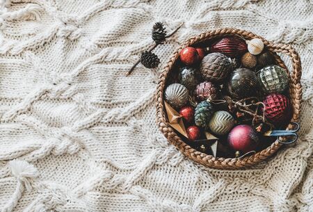 Christmas or New Year holiday background, texture, wallpaper. Flat-lay of Christmas glass festive decoration toys and balls in basket over white knitted woolen background, top view, copy spaceの写真素材