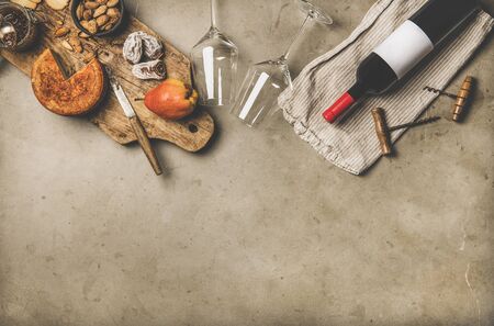 Wine and snack set. Flat-lay of wine bottle with blank label, vintage corkscrews, wineglasses, cheese and appetizers on board over grey concrete background, top view, copy space. Party food conceptの写真素材