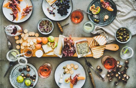 Mid-summer picnic with wine and snacks. Flat-lay of charcuterie and cheese board, rose wine in bottle and glasses, nuts, olives and fruits over concrete table background, top viewの写真素材