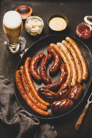 Octoberfest dinner table concept with grilled veal and pork sausages, sauce in jar, pickled vaggies and beer in glass over dark background, top viewの写真素材