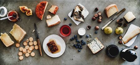 Wine and snack variety. Flat-lay of cheeses, honey, fruit, nuts, crackers, wine in glass and bottle over grey concrete background, top view. Gathering, holiday, party food conceptの写真素材