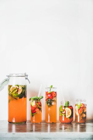 Homemade strawberry and basil lemonade or ice tea in glass and tumblers with eco-friendly plastic-free straws on grey concrete table, white wall at background, copy space. Cold refreshing soft drinkの写真素材