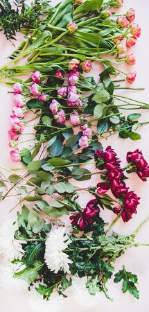 Various summer flowers flat-lay. Purple peonies, pink roses and tulips, white chrysanthemums and green branches with leaves over pastel pink background, top viewの写真素材