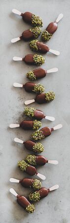 Ice cream pattern. Flat-lay of chocolate glazed ice cream pops with pistachio icing over grey...