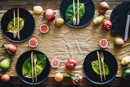 Autumn table styling for holiday dinner. Flat-lay of black dinnerware with fruit and fallen leaves...