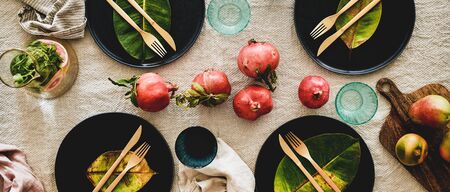 Autumn table styling for holiday dinner. Flat-lay of dinnerware with fruits and fallen leaves for decoration over beige linen tablecloth, top view, wide composition. Preparation for Thanksgiving dayの写真素材