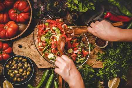 Flat-lay of womans hands mixing Turkish Chopard Salad made of fresh vegetables, herbs with olives and spices on plate, top view. Middle eastern, Mediterranean typical cuisine, vegan healthy dishの写真素材
