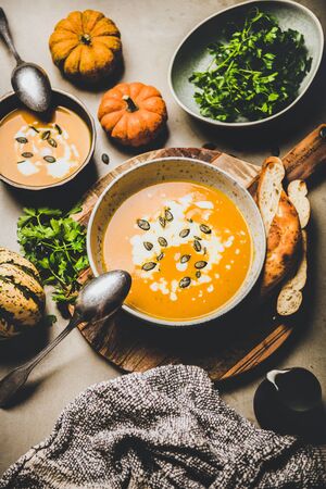 Autumn, winter warming seasonal meal. Flat-lay of pumpkin soup with seeds, parsley and cream in bowls over grey concrete background, top view. Vegan, vegetarian, healthy, comfort food conceptの写真素材