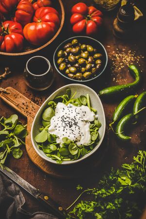 Turkish starter, meze dish. Bowl of fresh green  salad with yogurt, black sesame over rusty table with vegetables and spices, top view.の写真素材