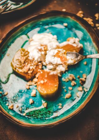 Turkish traditional pumpkin dessert. Flat-lay of pumpkin in sweet syrup with cinnamon, walnuts, whipped cream in fork, top view, selective focus. Middle East oriental cuisine typical vegan foodの写真素材