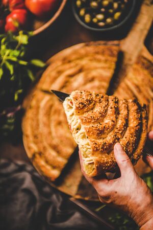 Turkish traditional pastry for breakfast. Human hands holding piece of borek pie with spinach filling and vegetable ingredients over rusty table background, top view, selective focus. Turkish cuisineの写真素材