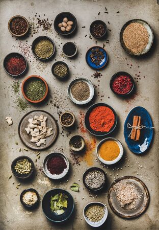 Flat-lay of spices in bowls and plates over grey background, top view. Black pepper, allspice, cloves, thyme, cumin, sesame, star anise, ginger, cinnamon, cardamom, mahlep, smoked salt, rosemary, bayの写真素材
