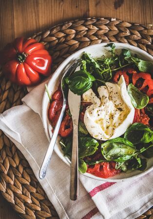 Flat-lay of traditional Italian salad with Buratta cheese, tomatoes, arugula and fresh basil on wooden table background, top view. Classical Italian cuisine conceptの写真素材