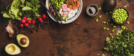 Flat-lay of salmon poke bowl or sushi bowl with vegetables, greens, sushi rice, soy sauce and...