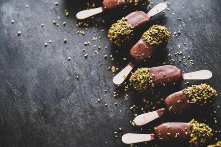 Ice cream pattern. Chocolate glazed ice cream pops with pistachio icing over dark background, selective focus, copy space. Summer seasonal cold sweet healthy vegan dessertの写真素材