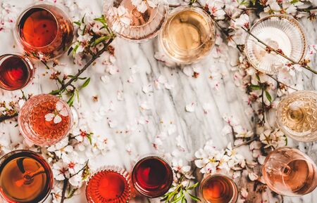 Flat-lay of rose wine of different colors in glasses and spring blossom flower over whiteの写真素材
