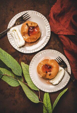 Flat-lay of Turkish traditional dessert with sweet quince boiled in sugar syrup and spices and heavy cream Kaymak on plates over rusty brown table background, top view. Turkish national cuisineの写真素材