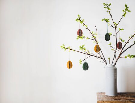 Easter holiday home decoration. Tree branches in vase with fresh spring leaves decorated with...