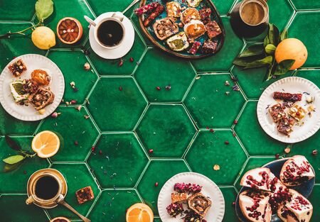 Flat-lay of variety of Turkish traditional lokum sweet delight with Turkish coffee in cups over green Moroccan tile table, top view, copy space. Middle East typical dessert foodの写真素材