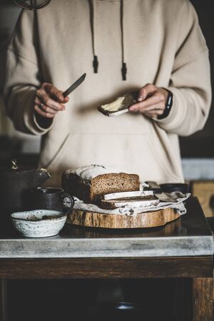 Woman having breakfast and spreading butter to healthy rye Swedish bread slice covered with flour in kitchen, selective focusの写真素材