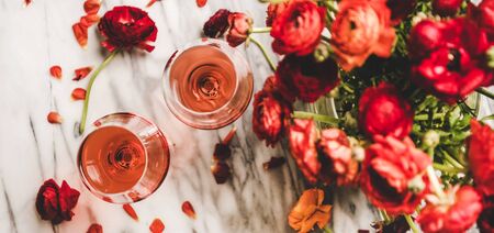 Flat-lay of rose wine in glasses and red spring blossom flowers bouquet over white marbleの写真素材