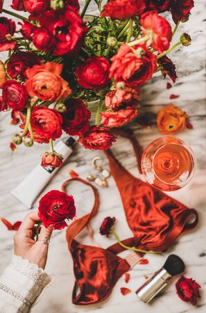 Female care beauty things. Flat-lay of silk lingerie, cosmetics, cream, jewelry, glass of rose wine and womans hand with red flower over marble table, top view. Feminine attributes and beauty ritualsの写真素材
