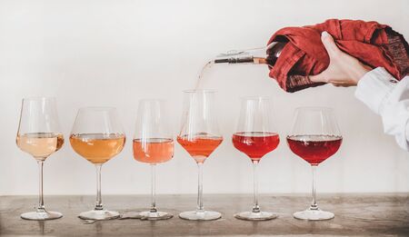 Shades of Rose wine in stemmed glasses placed in line and womans hand pouring wine from bottle to glassの写真素材