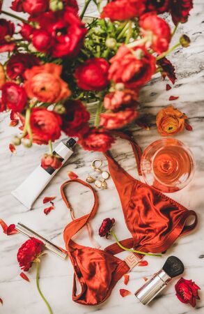Female care beauty things. Flat-lay of womens silk lingerie, cosmetics, cream, jewelry, glass of rose wine and red flowers over marble background, top view. Feminine attributes and beauty ritualsの写真素材