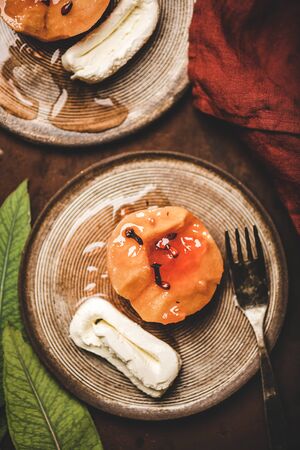 Flat-lay of turkish traditional dessert with sweet quince boiled in sugar syrup, spices and cream Kaymak on ceramic plates over rusty brown table background, top view. Turkish national cuisineの写真素材