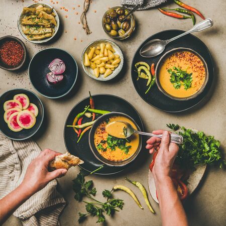 Flat-lay of turkish lentil soup Mercimek , vegetables, flatbread, pickled pepper and man eating from spoon over concrete background, top view, square crop. Vegetarian, Oriental, Middle Eastern cuisineの写真素材
