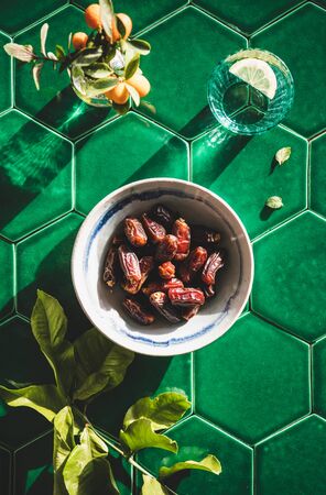 Flat-lay of dates in bowl and fresh drinking water with lemon in glass over greenの写真素材