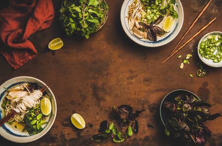 Vietnamese cuisine lunch. Flat-lay of rice noodle chicken soup Pho Ga with cilantro, soy sprouts, greens, lime in bowls with wooden chopsticks over rusty background, top view, copy spaceの写真素材