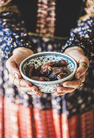 Woman in oriental dress holding bowl of dates in hands for Ramadan iftar evening meal and fasting month.の写真素材