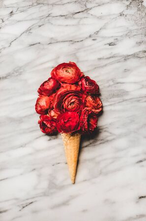 Flat-lay of ice cream waffle cone with scoop of red blooming ranunculus flowers over white marble table background. Seasonal spring or summer natural dessert conceptの写真素材