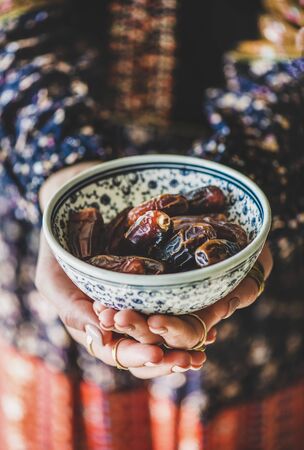 Woman in oriental dress holding bowl of dates in hands for Ramadan iftar evening meal.の写真素材