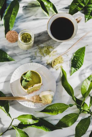 Flat-lay of green matcha cheesecake and black coffee in cup on grey marble tableの写真素材
