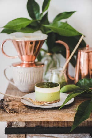 Coffee and dessert setup. Green matcha cheesecake and black coffee in copper pot and cup on rustic wooden kitchen counter, white wall background, close-up. Healthy, vegan, vegetarian, low calorie foodの写真素材