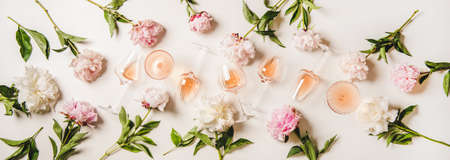 Rose wine variety layout. Flat-lay of rose wine in various glasses and summer blooming peony flowers over white background, top view. Summer drink for party, wine shop or wine tasting conceptの写真素材