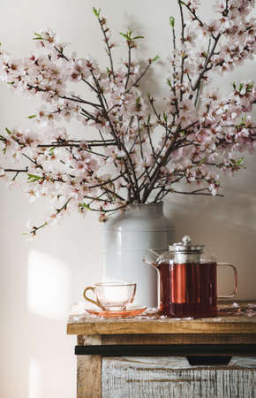 Hot black tea on rustic wooden cupboard under blooming almond tree branches in vase, white wall at backgroundの写真素材