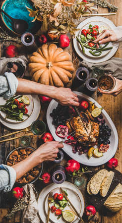 Thanksgiving party table setting. Flat-lay of people eating and celebrating holiday at table with roasted chicken, vegetables, fig pie, fruit, candles, tableware over wooden table background, top viewの写真素材