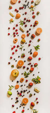 Fresh summer fruit and berries variety layout. Flay-lay of peaches, apricots, cherries, strawberries, blueberries, oranges and limes over plain white background, top view, vertical compositionの写真素材