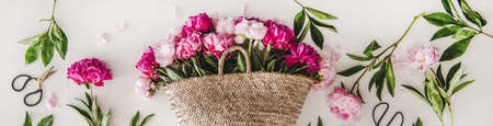 Summer flowers layout. Flat-lay of pink and purple peony flowers in basket over plain white background, top view, wide composition. Florist shop website banner or wallpaperの写真素材