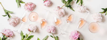 Rose wine variety layout. Flat-lay of rose wine in glasses and summer peony flowers over white background, top view. Summer drink for party, wine shop or wine tasting conceptの写真素材