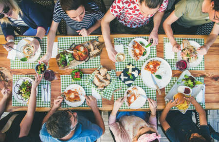 Family or friends summer party or outdoor dinner. Flat-lay of group of people at big table in cafe eating verious food together. Summer gathering or celebration conceptの写真素材