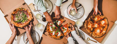 Pizza party for friends or family. Flat-lay of pizzas in boxes, lemon drinks and peoples hands cutting pizzas over white table background, top view. Fast food, comfort food, Italian cuisine conceptの写真素材