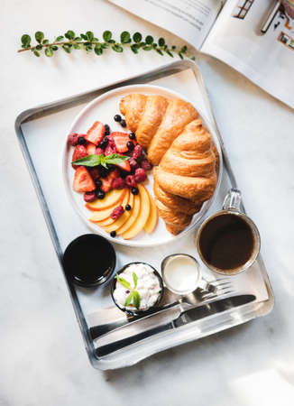 French breakfast cafe table setting. Flat-lay of breakfast with croissant, fresh berries, peach, cream cheese, jam and black coffee over white marble table background, top view. Comfort food conceptの写真素材
