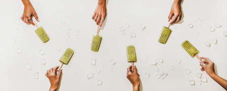 Green matcha coconut vegan ice cream  . Flat-lay of womens hands with matcha  over white table, top view. Summer vegetarian healthy dessert, clean eating, dairy free food conceptの写真素材